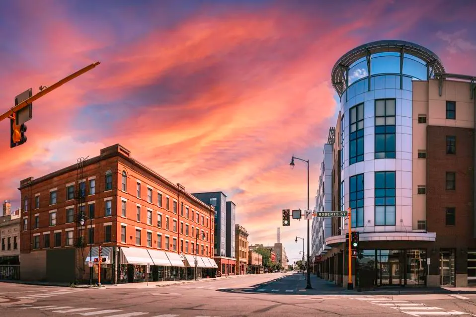 A city street in North Dakota at sunset with modern and historic buildings.