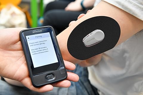 A person using a Dexcom CGM device, with a sensor attached to their arm and a handheld receiver displaying a pairing message.